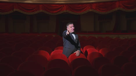 hombre feliz en la oscura sala de teatro vacía. hombre rico en traje de pie entre los sillones rojos vacantes en el gran auditorio y bailando alegremente solo.