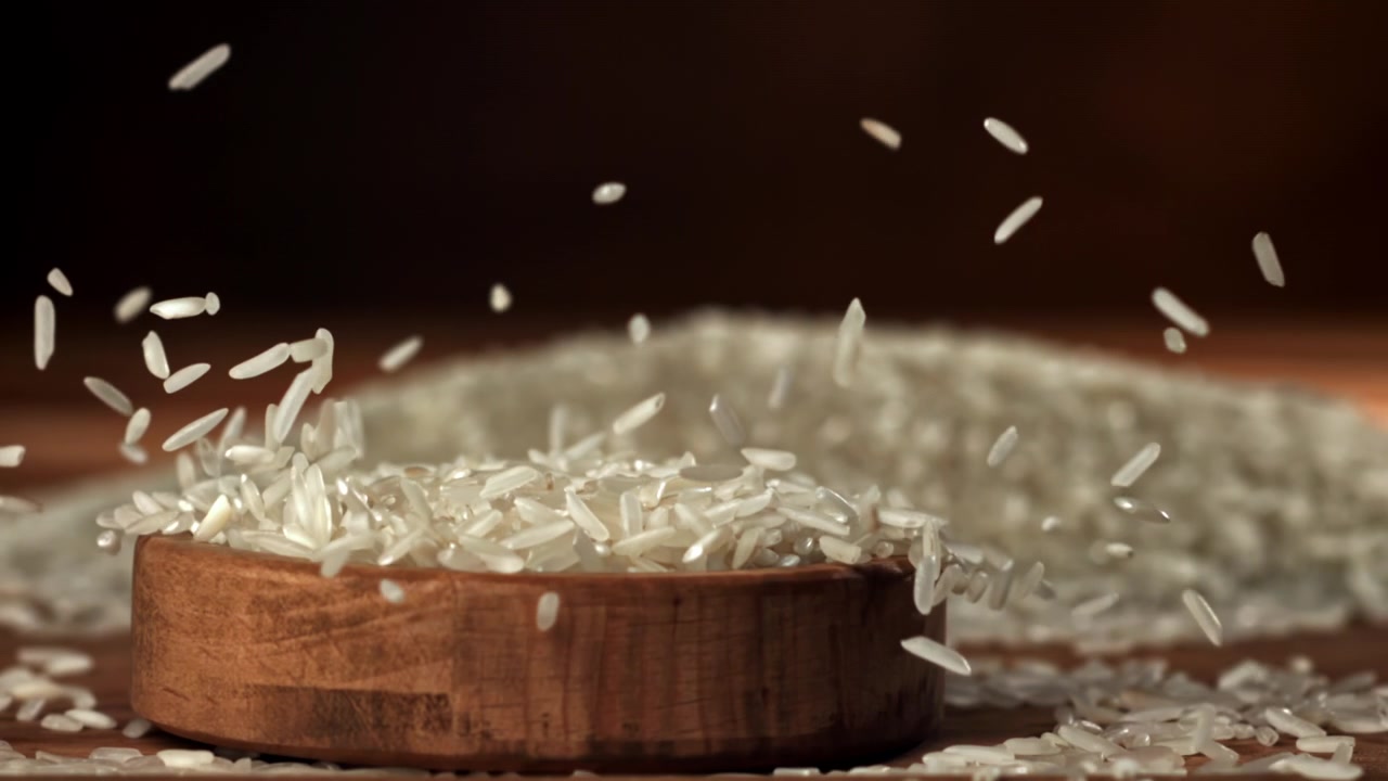 Chicchi di riso bianco che cadono al rallentatore in una ciotola di legno