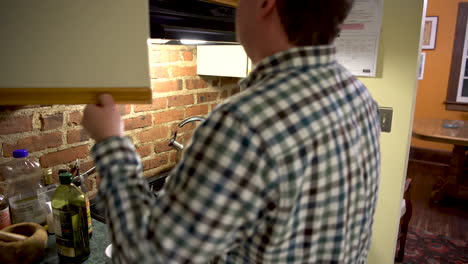 lost white male looks through kitchen cabinets for a plate, then attempt to take something out of the oven but burns himself, like an idiot