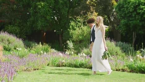 Happy-diverse-couple-walking-in-garden-on-sunny-day-at-wedding