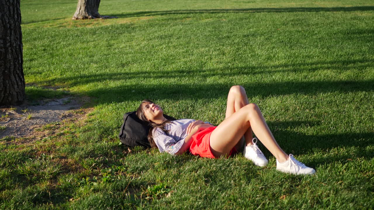 A beautiful young woman resting in the grass field of a public park daydreaming on a warm summer sunny day SLOW MOTION