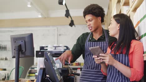 video of happy diverse female and male waiters in aprons working with tabelet at coffee shop