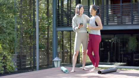 Glückliche-Asiatische-Freundinnen-Mit-Wasserflasche-Und-Smartphone-Lachen-Auf-Der-Terrasse,-Zeitlupe