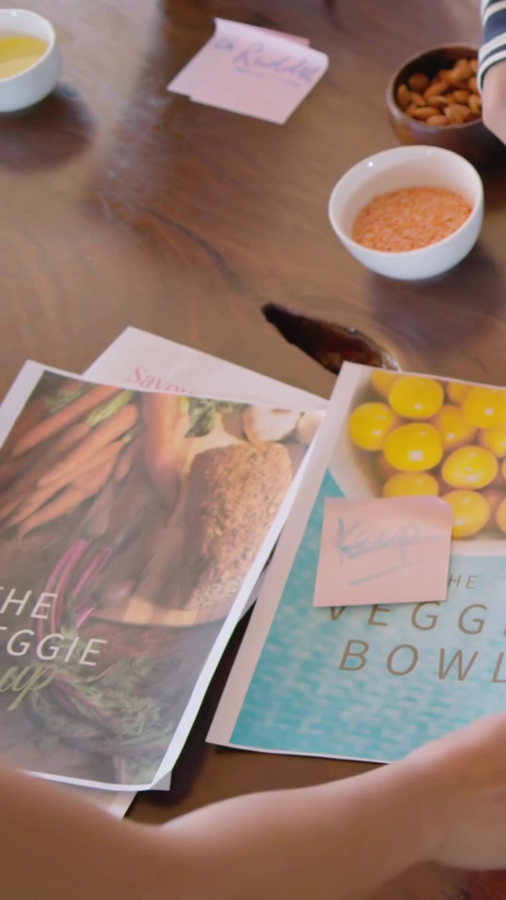 Vídeo vertical: Adulto e criança inclinados, organizando páginas de receitas na mesa de jantar, adicionando anotações rosas