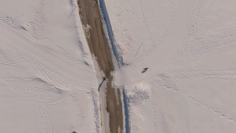 aerial drone shot of a man cross-country skiing with his dog crosses a road -- orbit shot