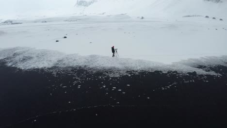 a beautiful drone shot of the black beach in iceland shows the high waves of the sea and the cloudy weather while the snow covers some of the black sand