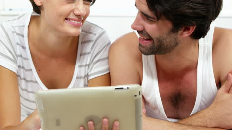 pareja linda acostada en la cama y mirando una tableta