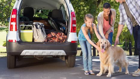 Happy-caucasian-parents-and-daughter-standing-beside-open-car-with-pet-dog-in-park