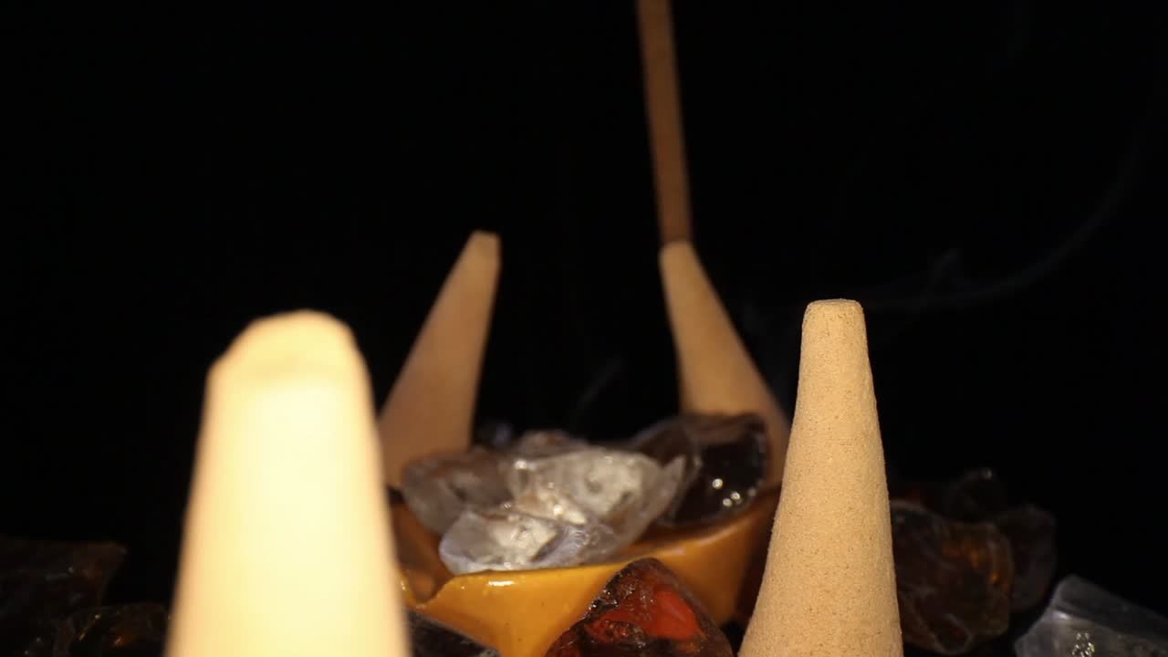 empujando varios conos de incienso apagados en un jardín de rocas decorativas, hacia un palo encendido con un pequeño humo ondulante