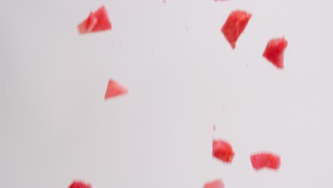 pink, juicy diced watermelon cube pieces raining down on white backdrop in slow motion