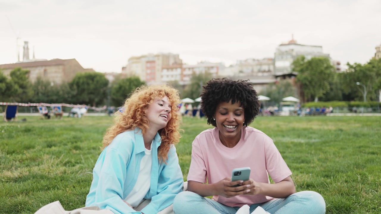 Happy Young Women Friends Laughing While Using Smartphone in Park