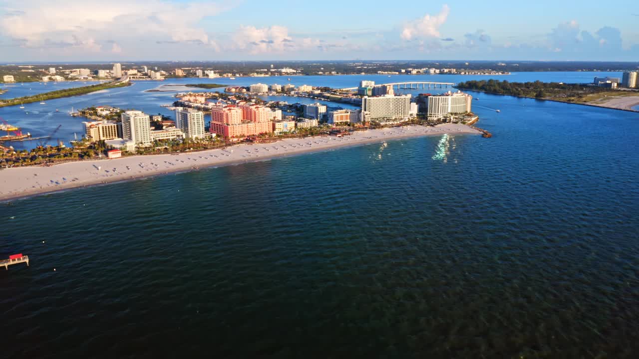 Colorful beachfront resorts line the sandy coast where a long pier stretches into the turquoise sea, capturing the lively atmosphere of a seaside urban landscape