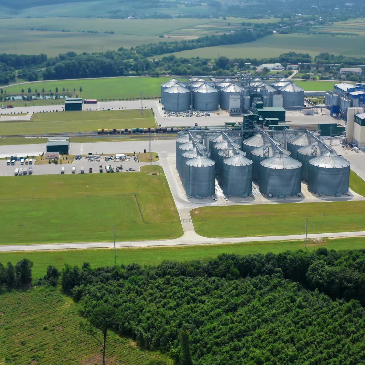 Grain elevators in agricultural zone. Granary with mechanical equipment for receiving, cleaning, drying grain. Modern agricultural complex surrounded with beautiful landscape. Aerial view