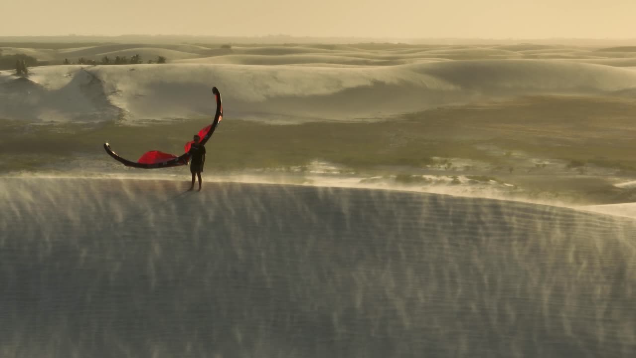 kitesurfer en la cresta de la cometa de dunas de arena en la mano, arena volando en condiciones de viento