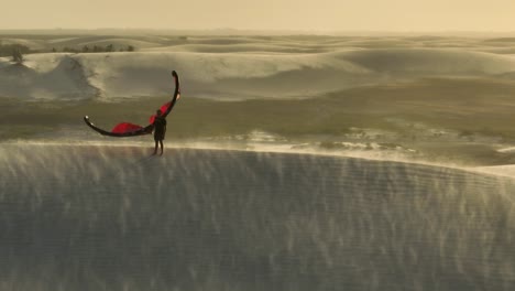 Kitesurfer-on-crest-of-sand-dune-kite-in-hand,-sand-flying-in-windy-conditions