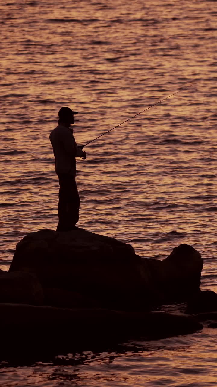 Fishermen on the rocks. Man's silhouette fishing at sunset. Freshwater fishing, catch of fish. Vertical video