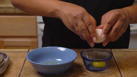 woman cracks open an egg in a bowl on the kitchen counter