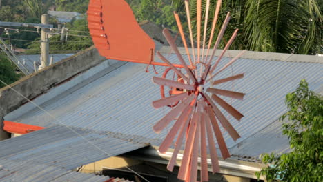 rust coloured spinning windmill with tin roofs in the background