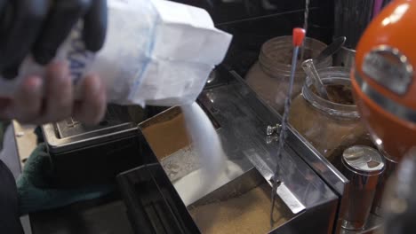 barista vertiendo azúcar llenando recipiente de acero inoxidable