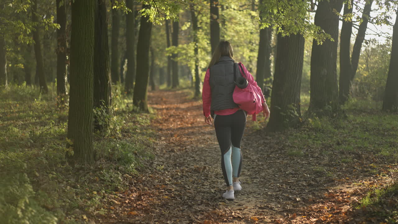 Woman Walking on a Leafy Forest Path in Sunlight