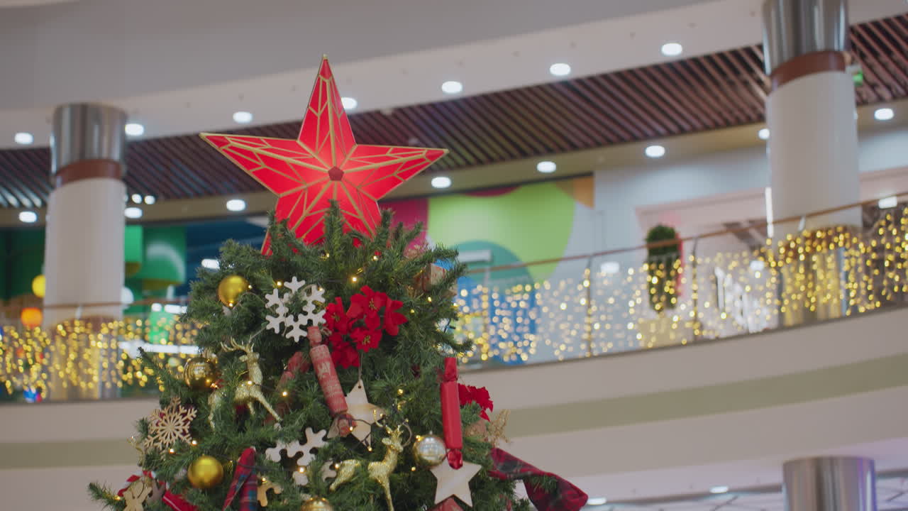 Close-up of beautifully decorated Christmas tree with glowing red star topper, golden ornaments, snowflakes, poinsettias, and festive decorations adorn lush green branches
