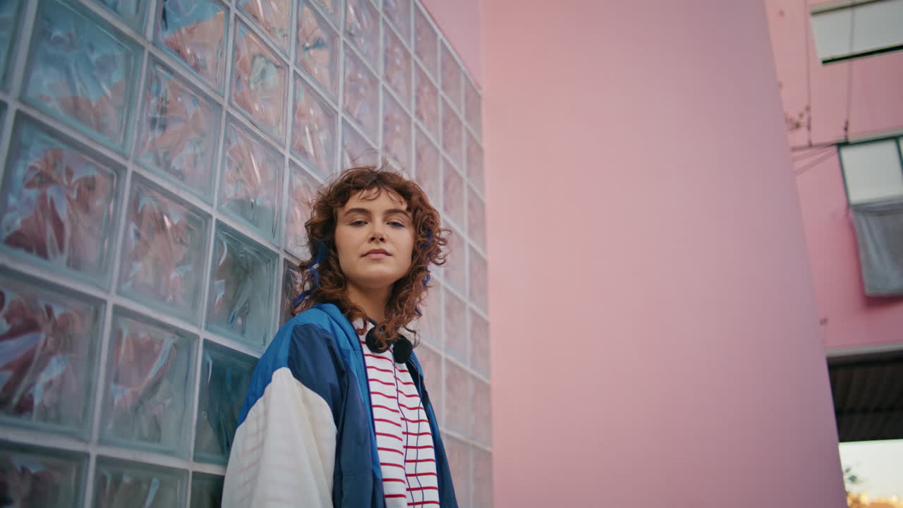 미소 짓는 십대 카메라가 유리 벽에 기대어 도시 건물을 확대합니다.