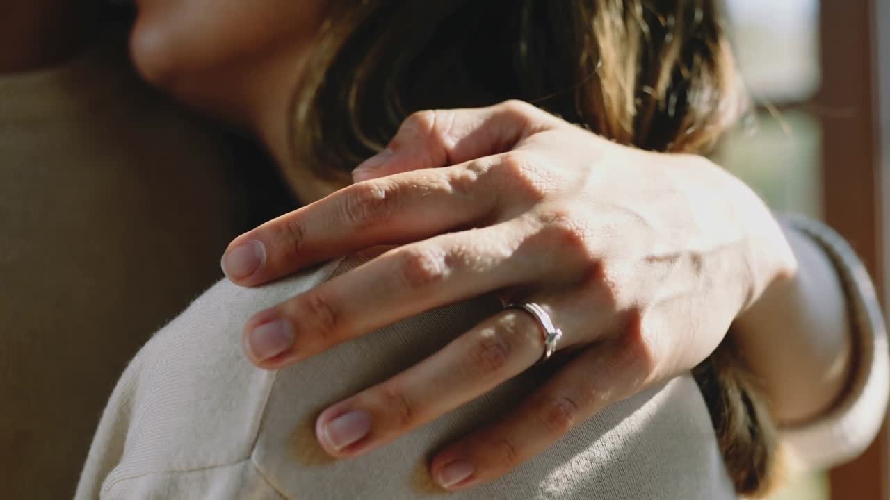 Settling partner's hand onto sweater shoulder at home by window, comforting, ring catching light