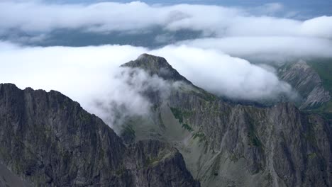 slow advection fog split by a mountain peak cascades down bare jagged slopes, the tatra mountains, time lapse