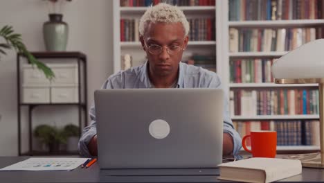 confident african american young man opens and start using laptop at home office