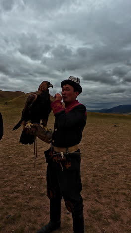 professional man holding golden eagle on his arm. cloudy landscape.