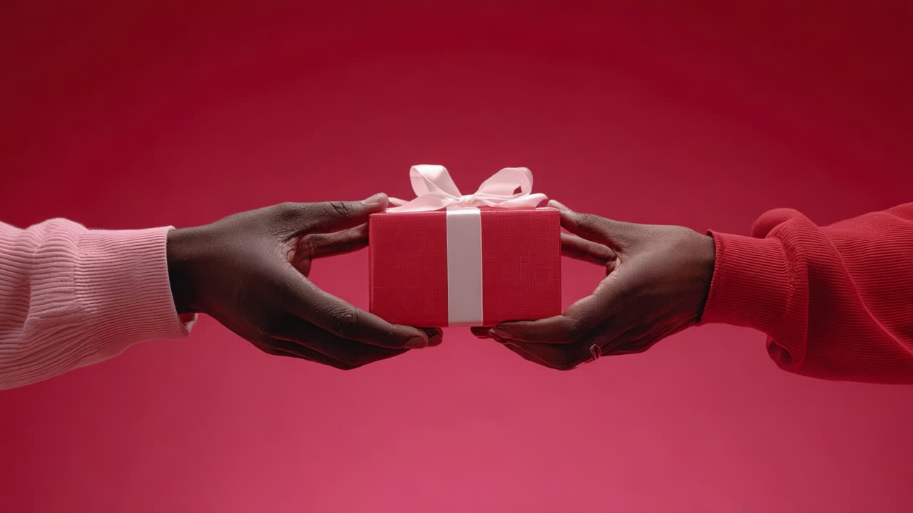 Un enternecedor momento de entrega: Dos manos extienden un regalo bellamente envuelto, que simboliza la conexión, la celebración y la alegría de compartir en una atmósfera roja radiante.