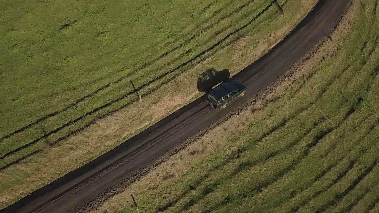슬로우 모션 공중 드론 뷰 클래식 wd suv가 잔디 사이에서 자갈 도로를 따라 운전합니다.