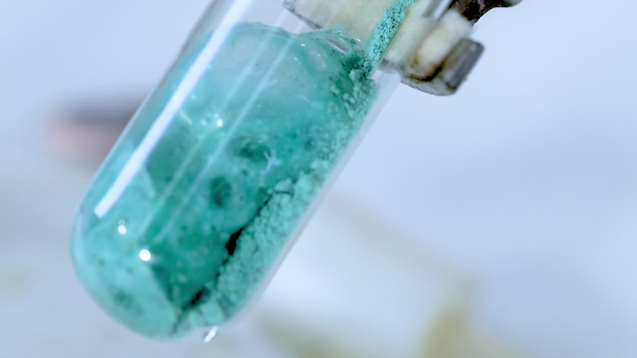 A sequence showing a green substance reacting and bubbling inside a test tube.