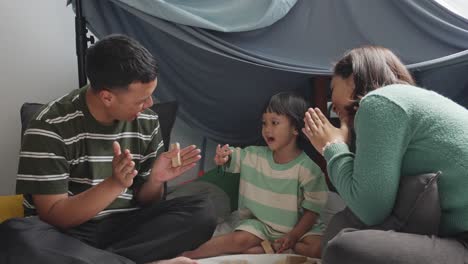 adorable little daughter learn to count number while father and mother clapped their hands, asian family spending quality time together in a tent at home