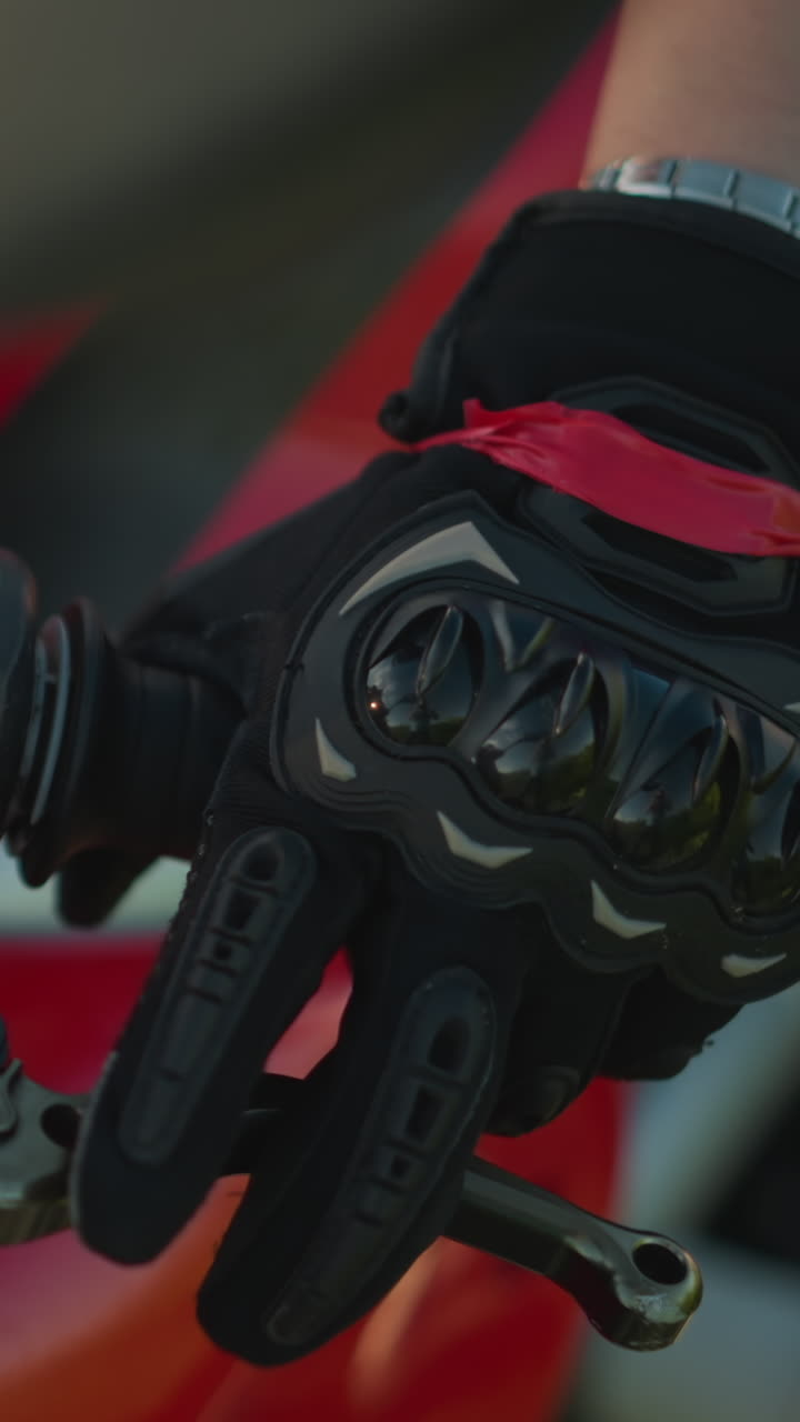 Close-up of a biker's hand wearing protective gloves while gripping the throttle and clutch lever on a motorcycle, the rider's wrist is adorned with a chain bracelet