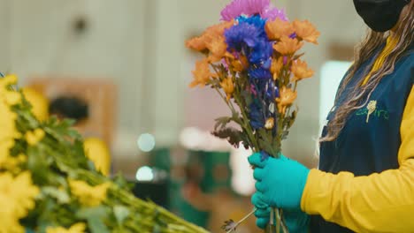 mujer florista en uniforme preparando ramos de flores de colores en una floristería industrial