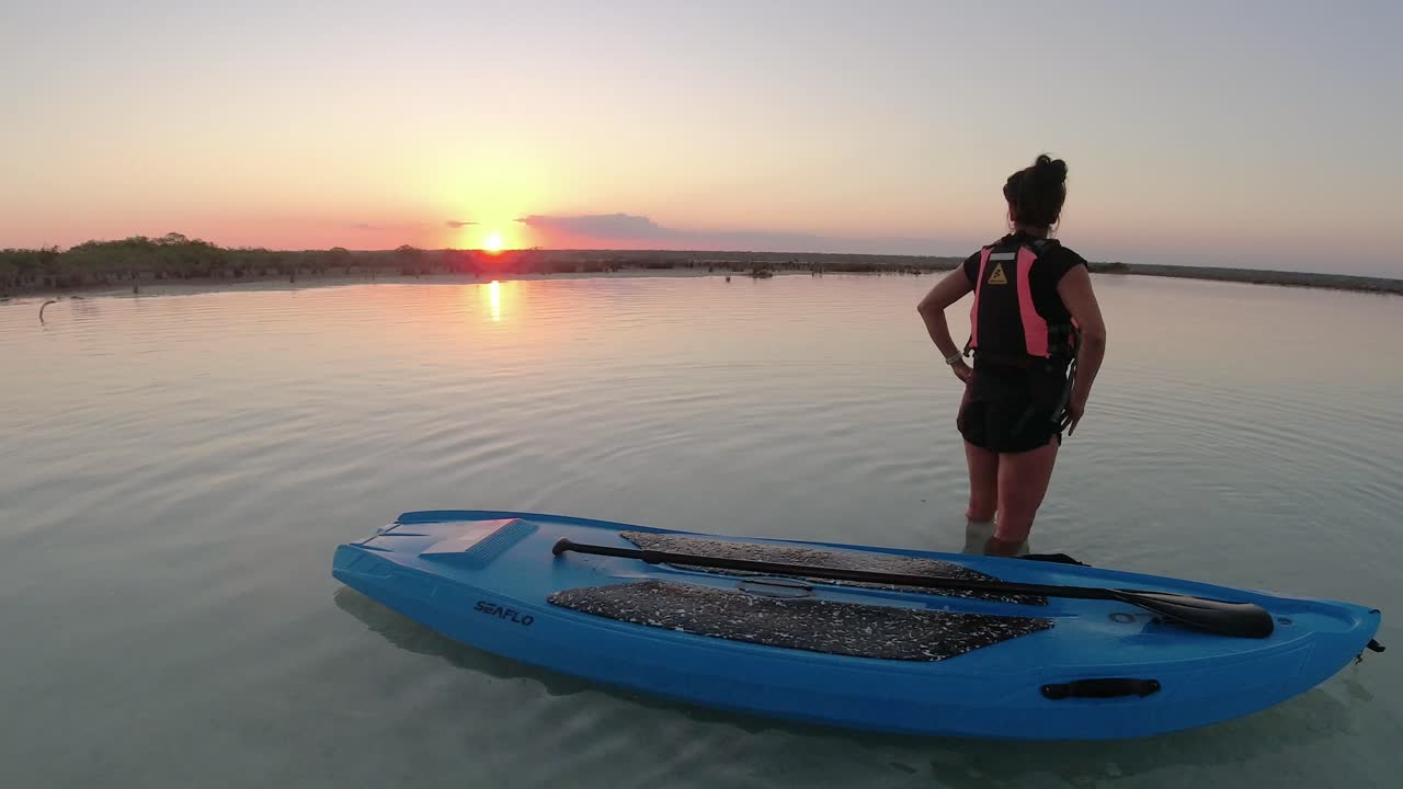 mujer joven sola disfrutando de la puesta de sol sobre un lago azul con tabla de remos en bacall méxico destino de vacaciones