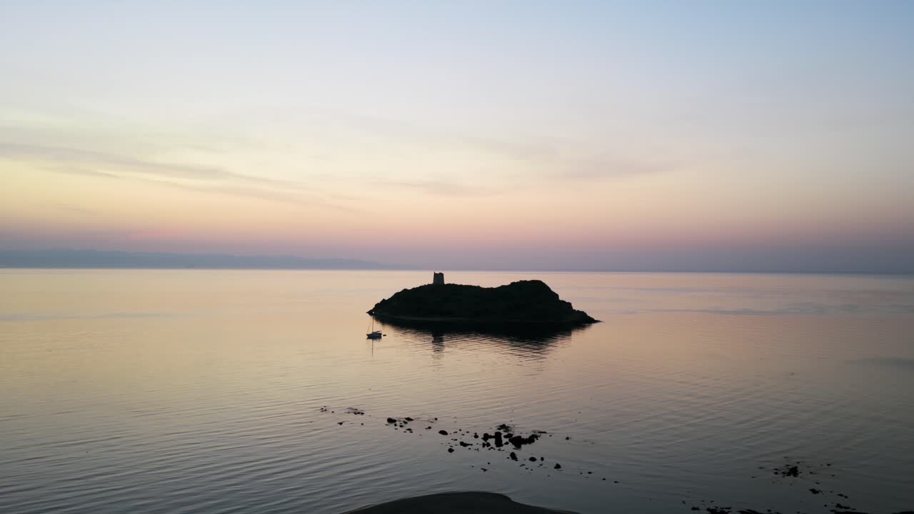 Serene seascape with an island, tower, and vibrant sunset colors in Sardinia. Aerial Dolly