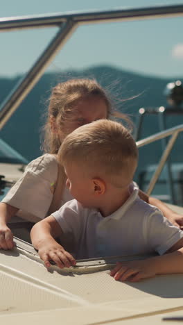 lovely little boy and girl look out of motorboat portal on sunny day. happy children siblings ready for sea cruise by yacht in ocean port on active vacation