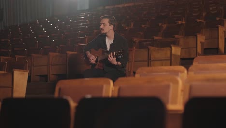 a handsome guy plays an acoustic guitar in an abandoned cinema. the musician sings a song and accompanies on the guitar