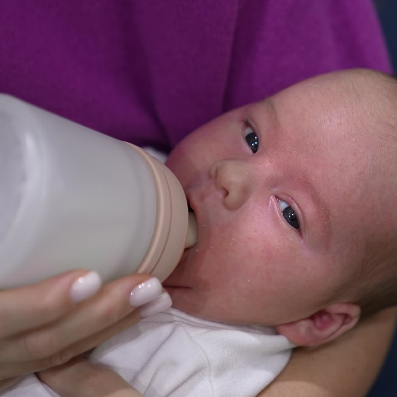 Adorable child in mother's hands ready to have meal. Little kid refuses to take the bottle first but then takes it and starts to eat. Close up