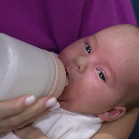 adorable child in mother's hands ready to have meal. little kid refuses to take the bottle first but then takes it and starts to eat. close up