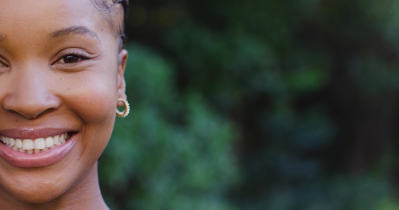 Mantenendo il contatto visivo, donna africana con il viso rilassato e sorridente nel parco con orecchini a cerchio d'oro, spazio per il testo