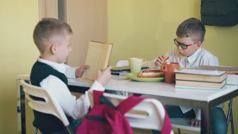 hungriger junge isst pizza und sein freund liest ein buch am weißen tisch