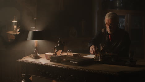 old passionate man writes down a note in his office at night
