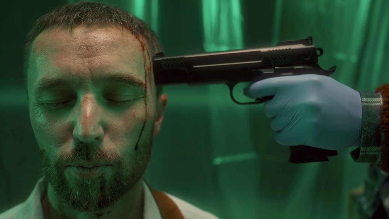 mano de un criminal con un arma en el templo de un cautivo con la cara ensangrentada