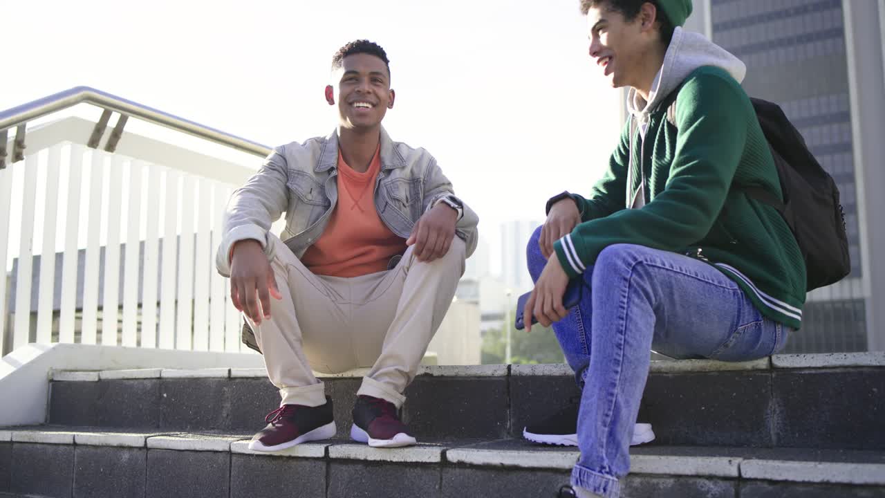 Amigos estudantes diversos sentados em degraus de concreto de uma praça mostrando a tela do smartphone e rindo.