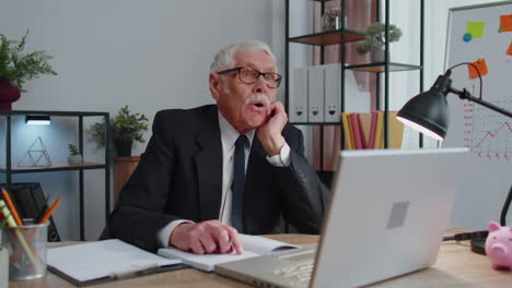 Senior-business-office-man-analyzes-financial-charts-celebrate-success-win-at-home-workplace-desk