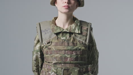 studio portrait of serious young female soldier in military uniform against plain background