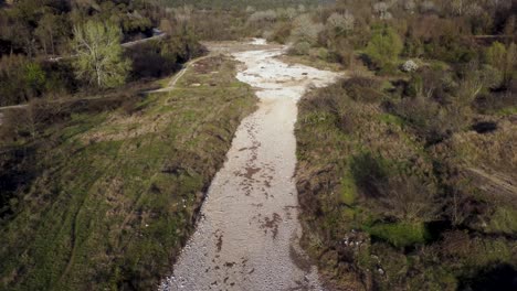 Dramatic-aerial-ascend-over-dry-river-surrounded-by-forests